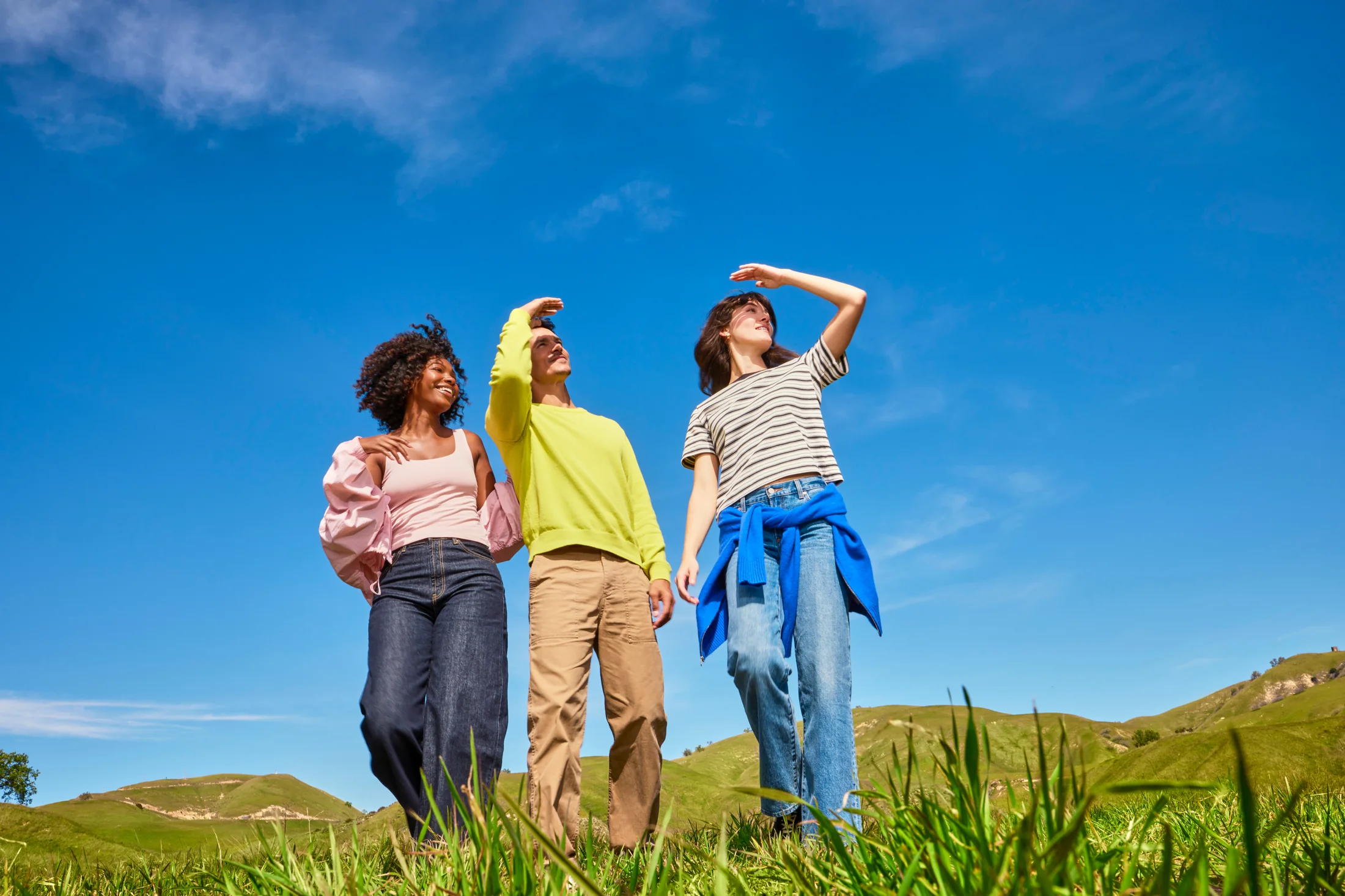 Three people looking up together under a bright blue sky